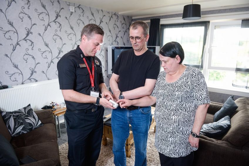 A fire officer showing a male and female a fire alarm in their living room